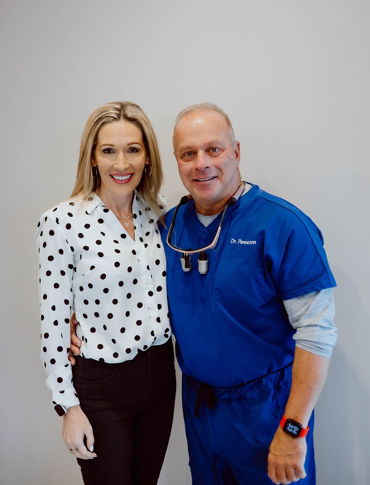 A man and a woman are posing for a picture together . the woman is wearing a polka dot shirt.