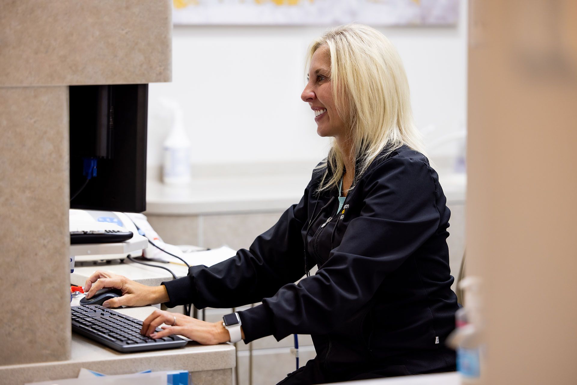A woman is sitting at a desk typing on a computer keyboard.