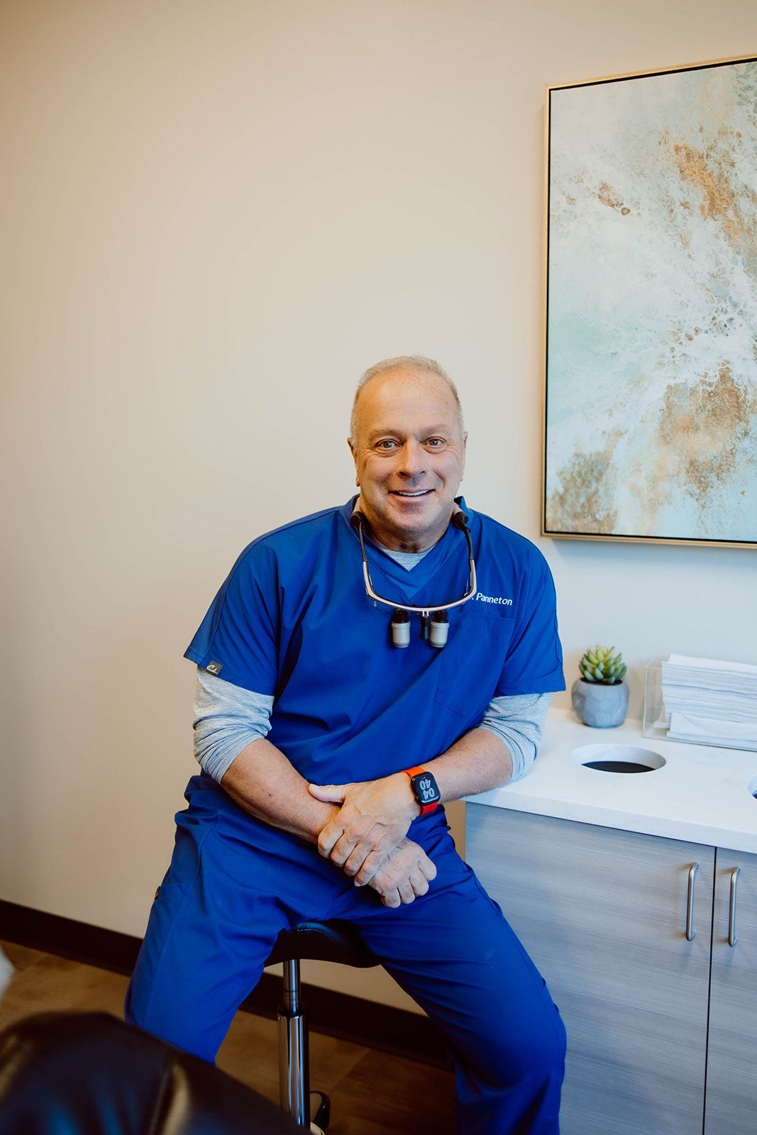 A man in a blue scrub is sitting on a stool in a room.