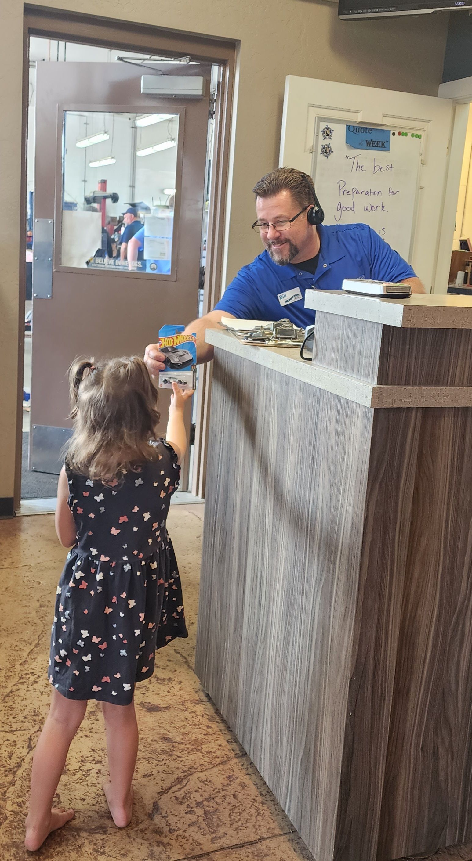 Child at a counter handing something to a man in a blue shirt inside a lobby.
