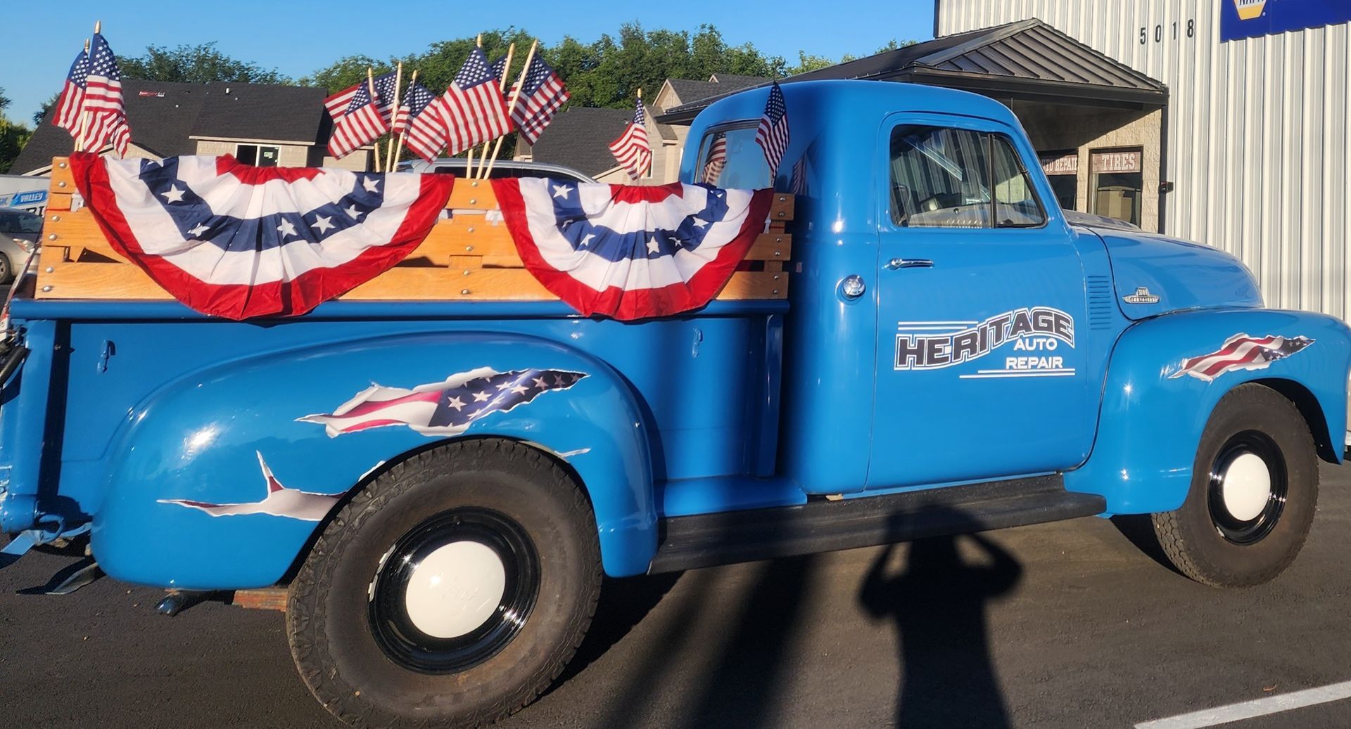 Blue vintage pickup truck decorated with red, white, and blue bunting and small American flags.
