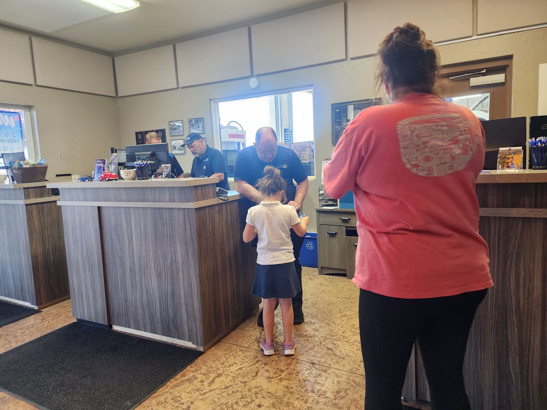 Child at a reception desk with an adult in a waiting area, seen from behind.