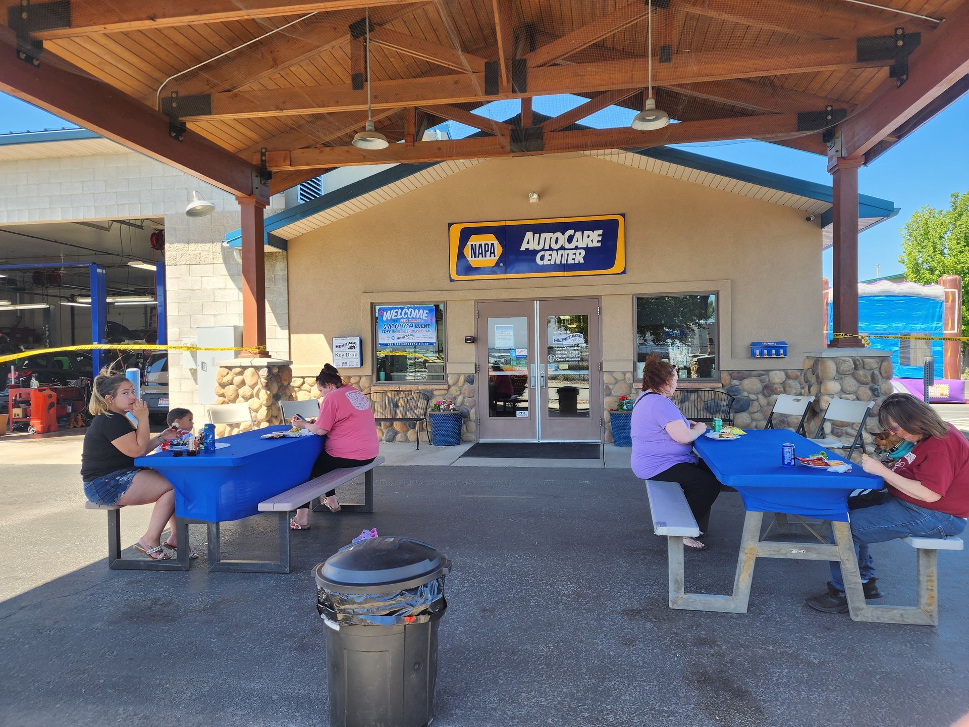 People seated at picnic tables outside a store under a wooden canopy.