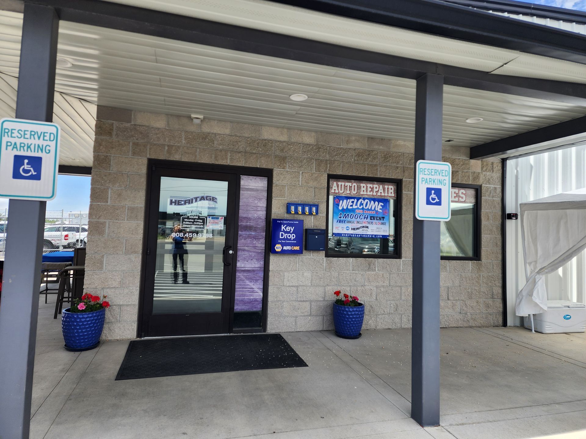 Accessible building entrance with glass door, blue handicap signs, and potted flowers under a covered walkway.