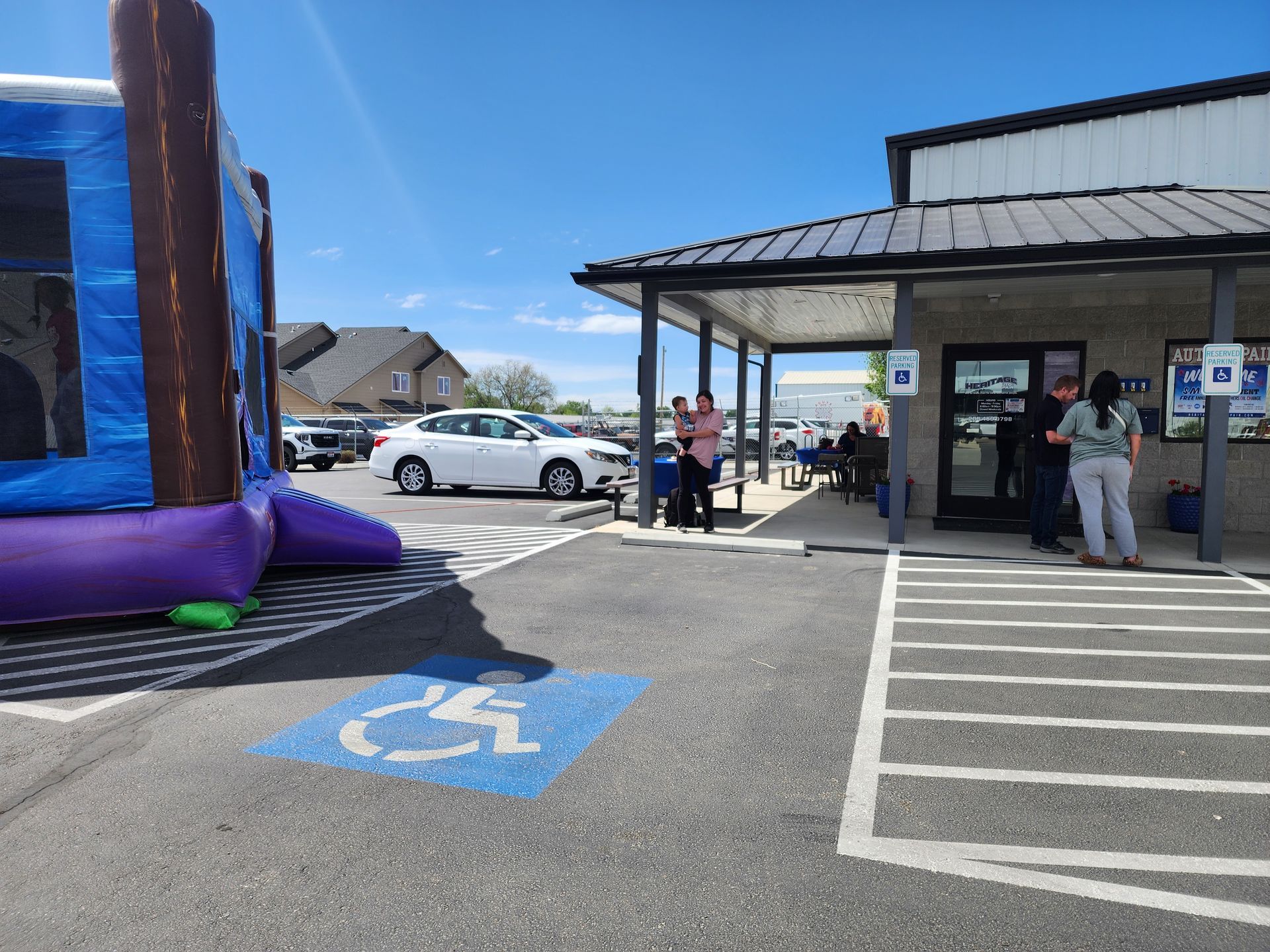 Outdoor storefront with a blue inflatable bounce house, parked cars, and people standing by the entrance.