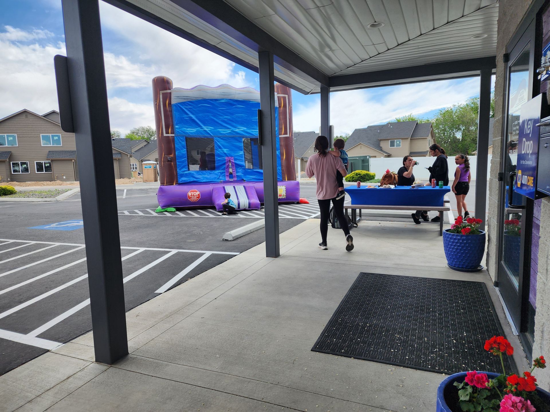 Covered sidewalk outside a blue bounce house, with people nearby on a wet street.