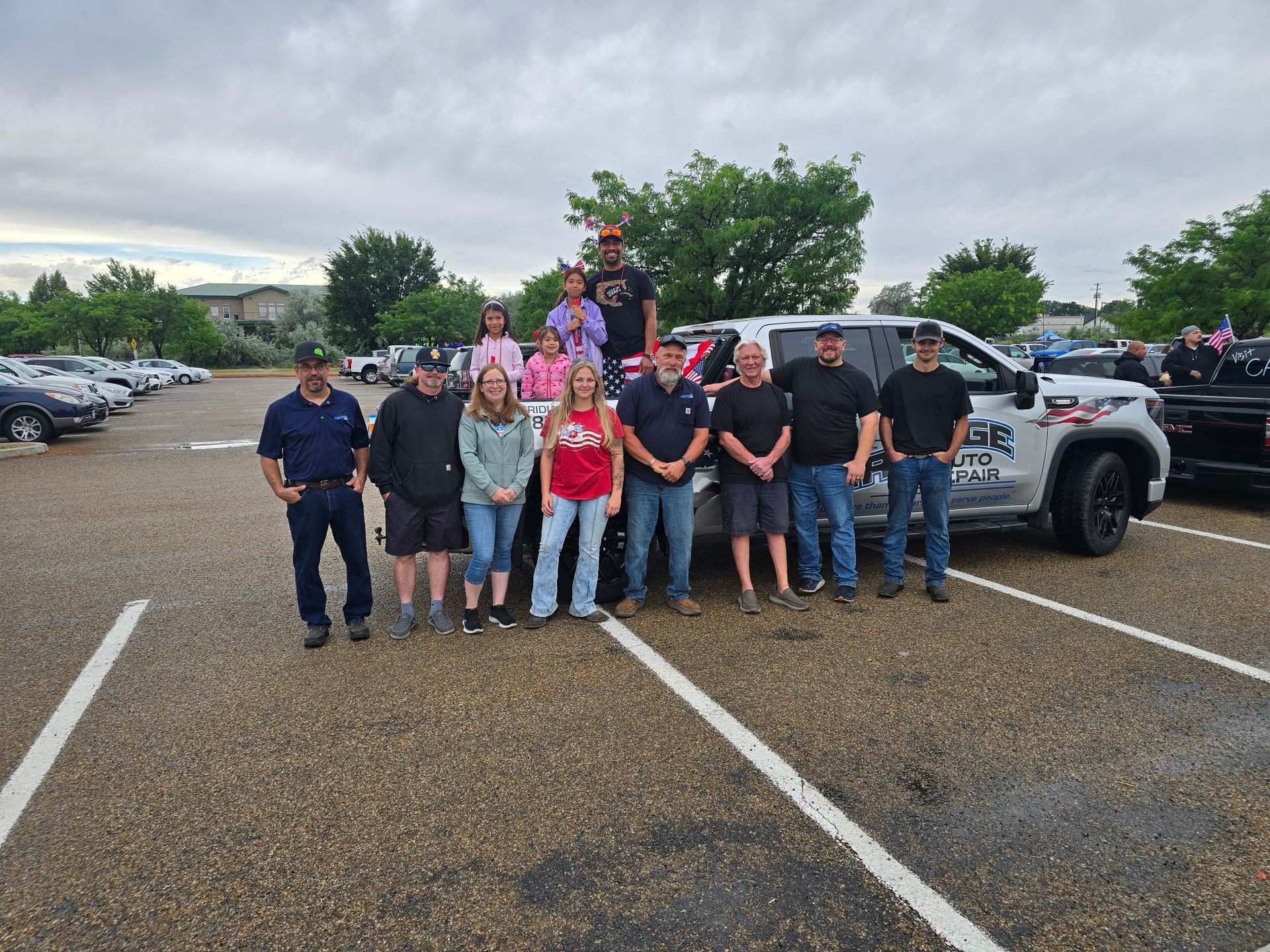 Group of people posing in a wet parking lot beside pickup trucks under a cloudy sky.