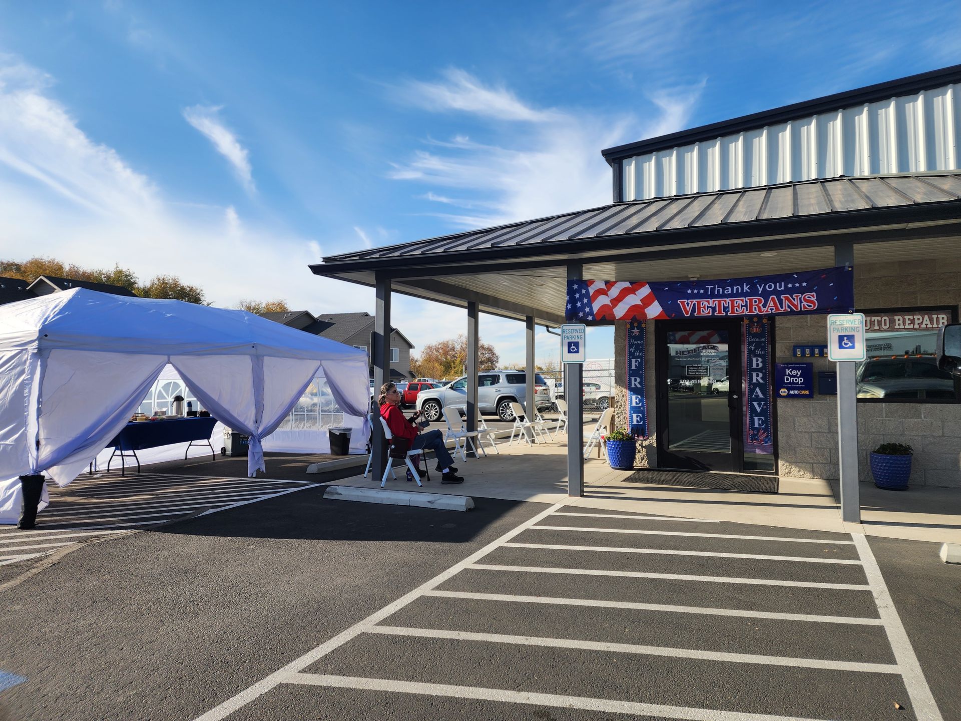 Parking lot event tent beside a storefront with a striped awning under a blue sky.