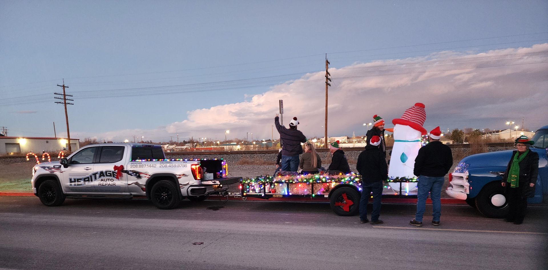 Decorated police car float in a parade at dusk, with people standing beside it and a cloudy sky.