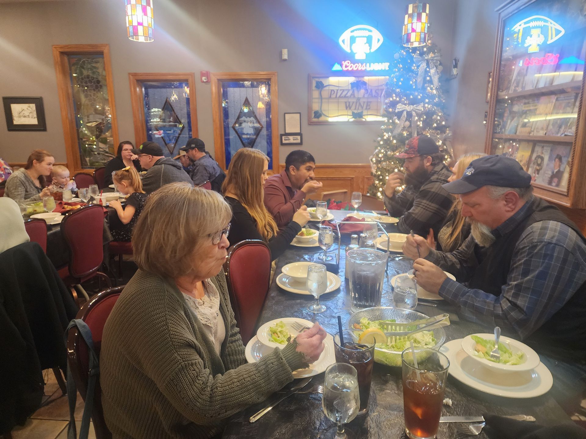 People dining at a warmly lit restaurant with tables, drinks, and holiday decorations.