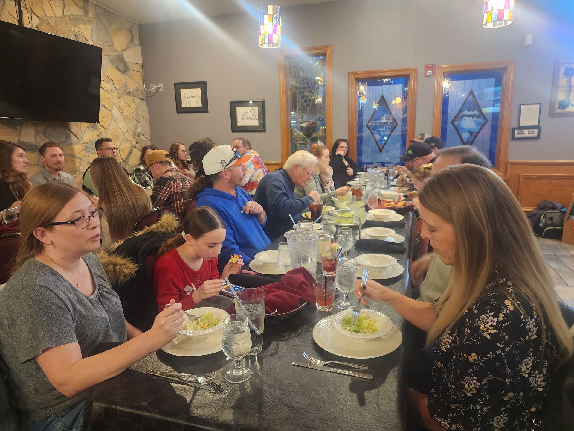 People seated at a long table sharing a meal in a warmly lit restaurant or banquet room.