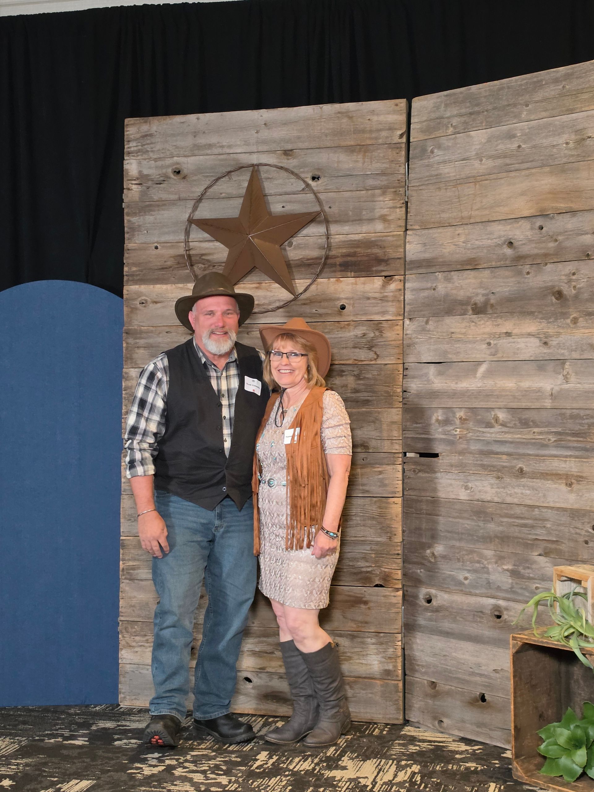 Two people standing before a rustic wooden wall with a large star decoration.