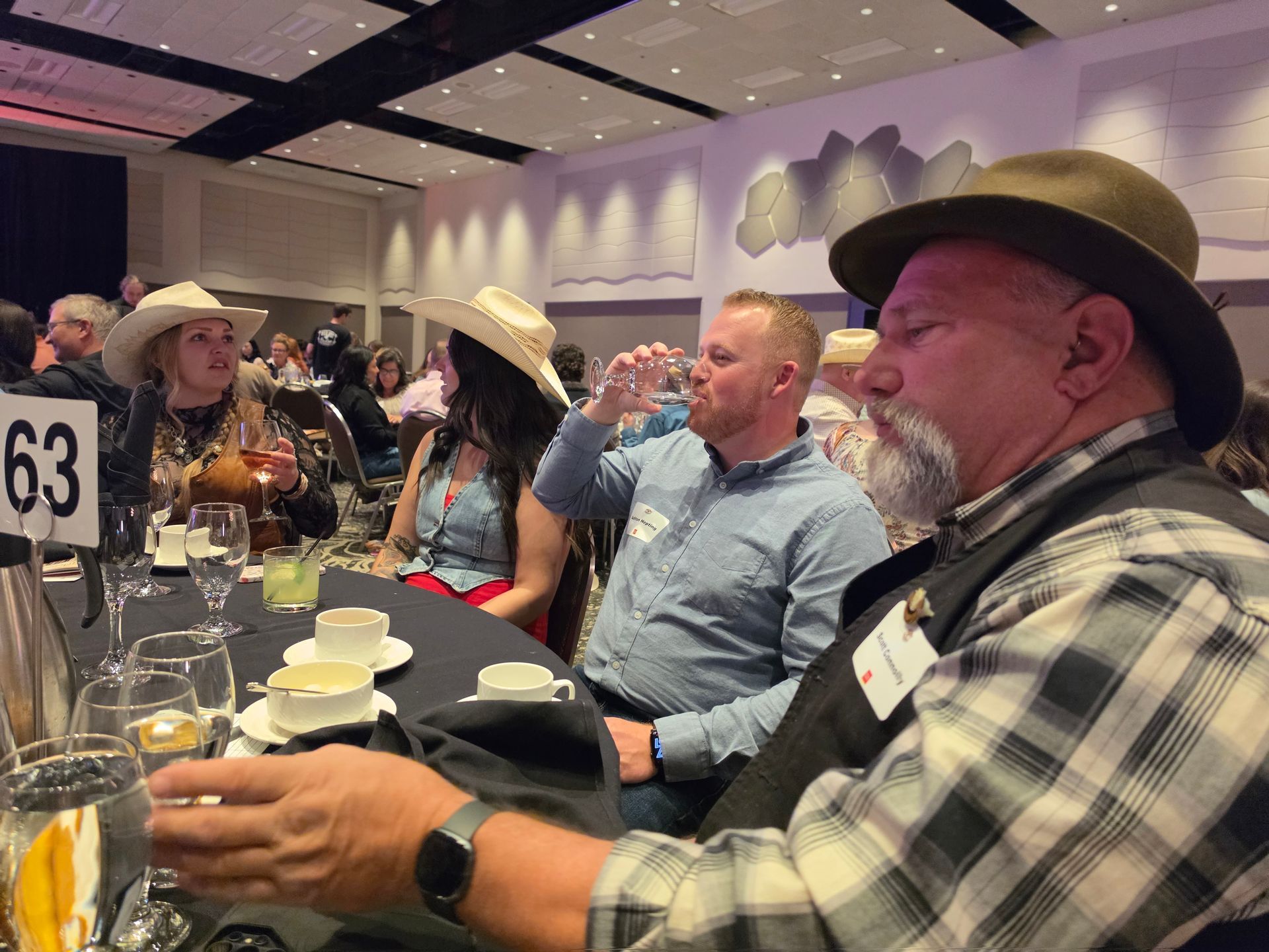 Cowboy hats at a banquet table with drinks and plates in a conference hall.