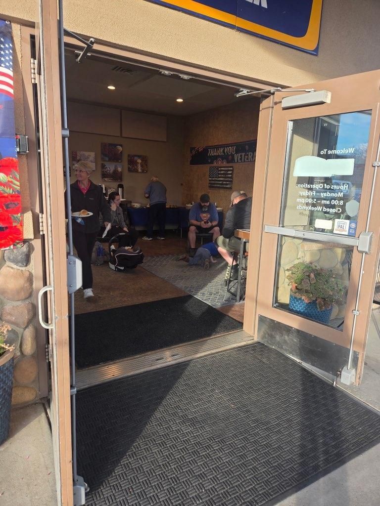 Open glass doors to a café entrance with people sitting inside and a black entry mat.
