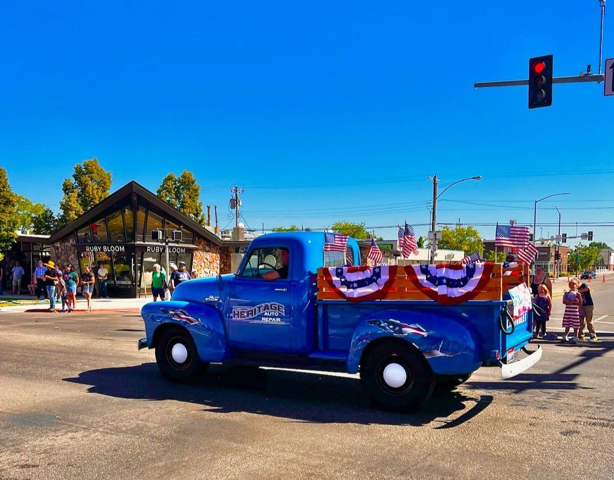 Blue vintage truck decorated with red, white, and blue bunting at a street parade under a traffic light.