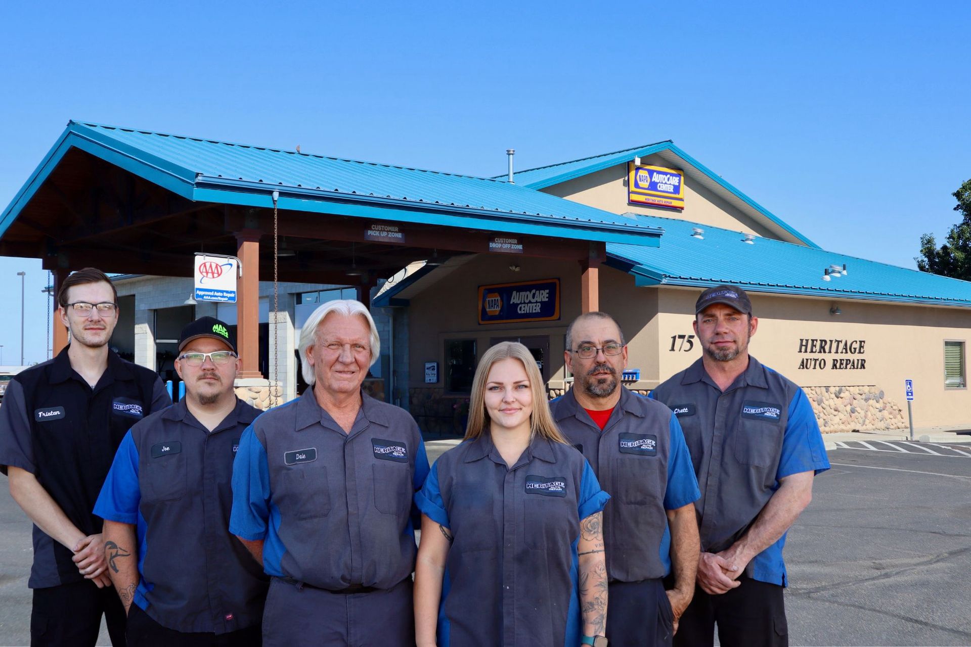 Six uniformed people standing outside a restaurant under a blue awning, posing together.