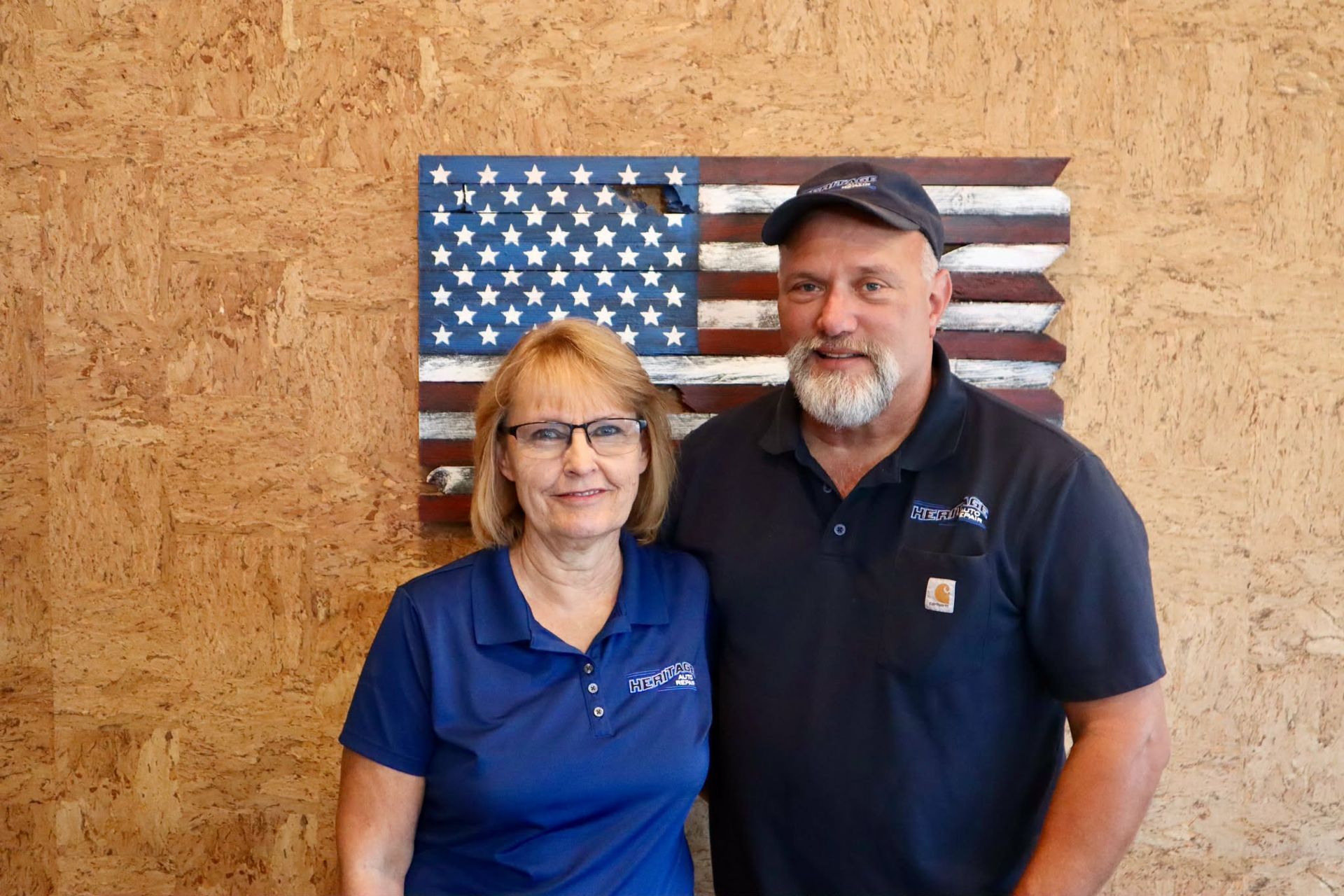 Two people posing in front of a rustic American flag wall hanging.