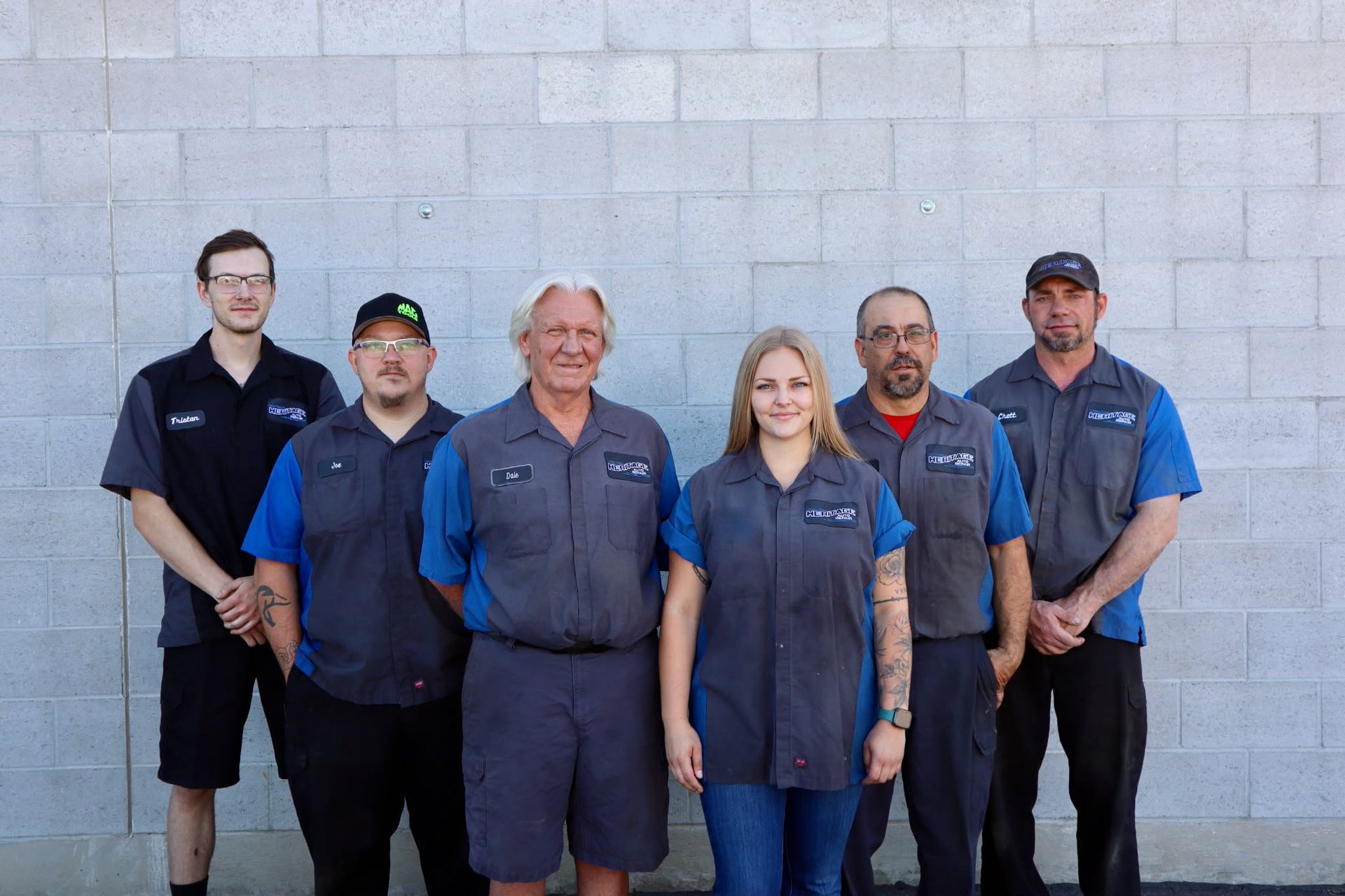 Six employees posing in matching work shirts against a gray wall.