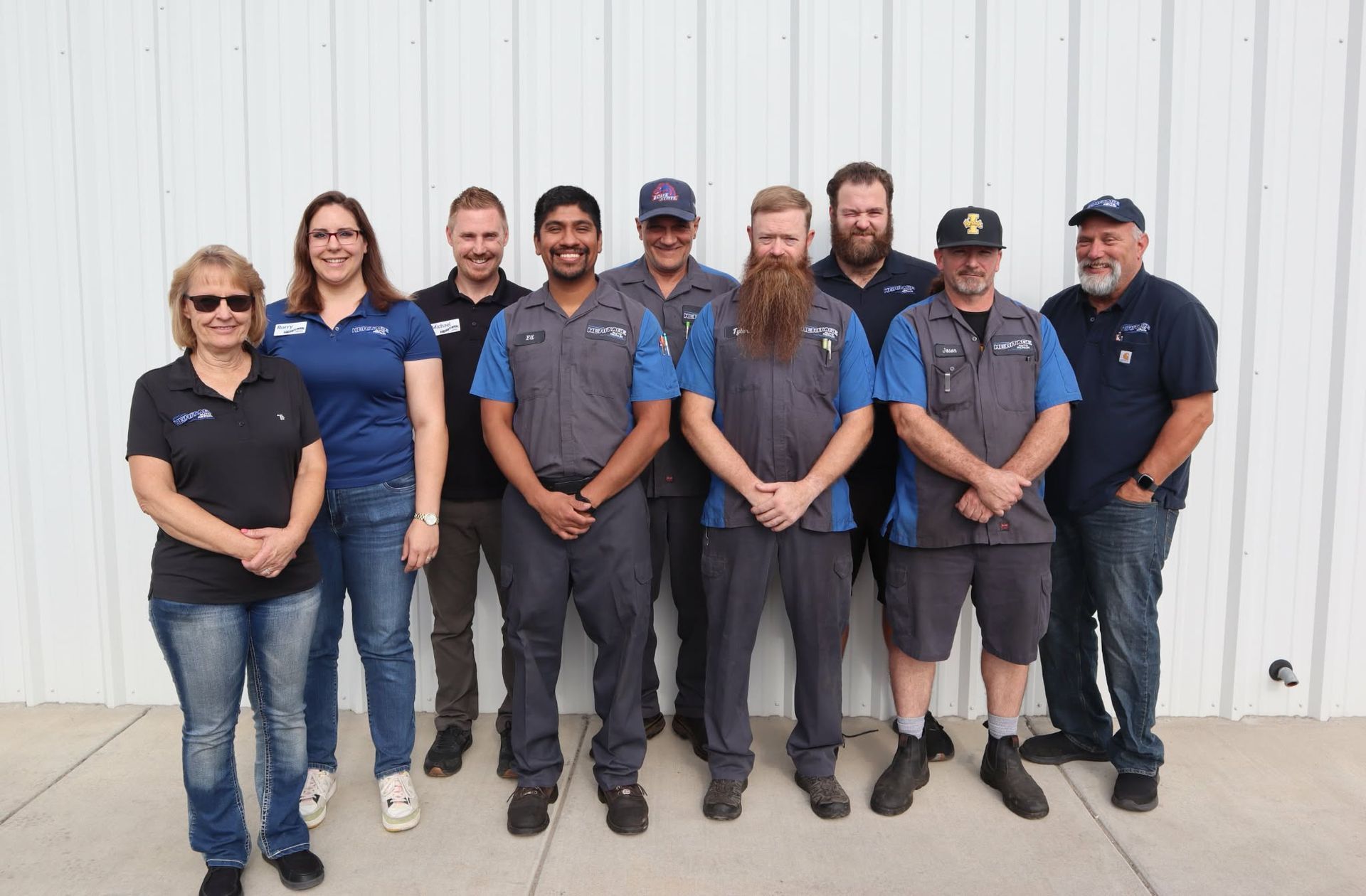 Group of eight staff members standing together in front of a white building wall.