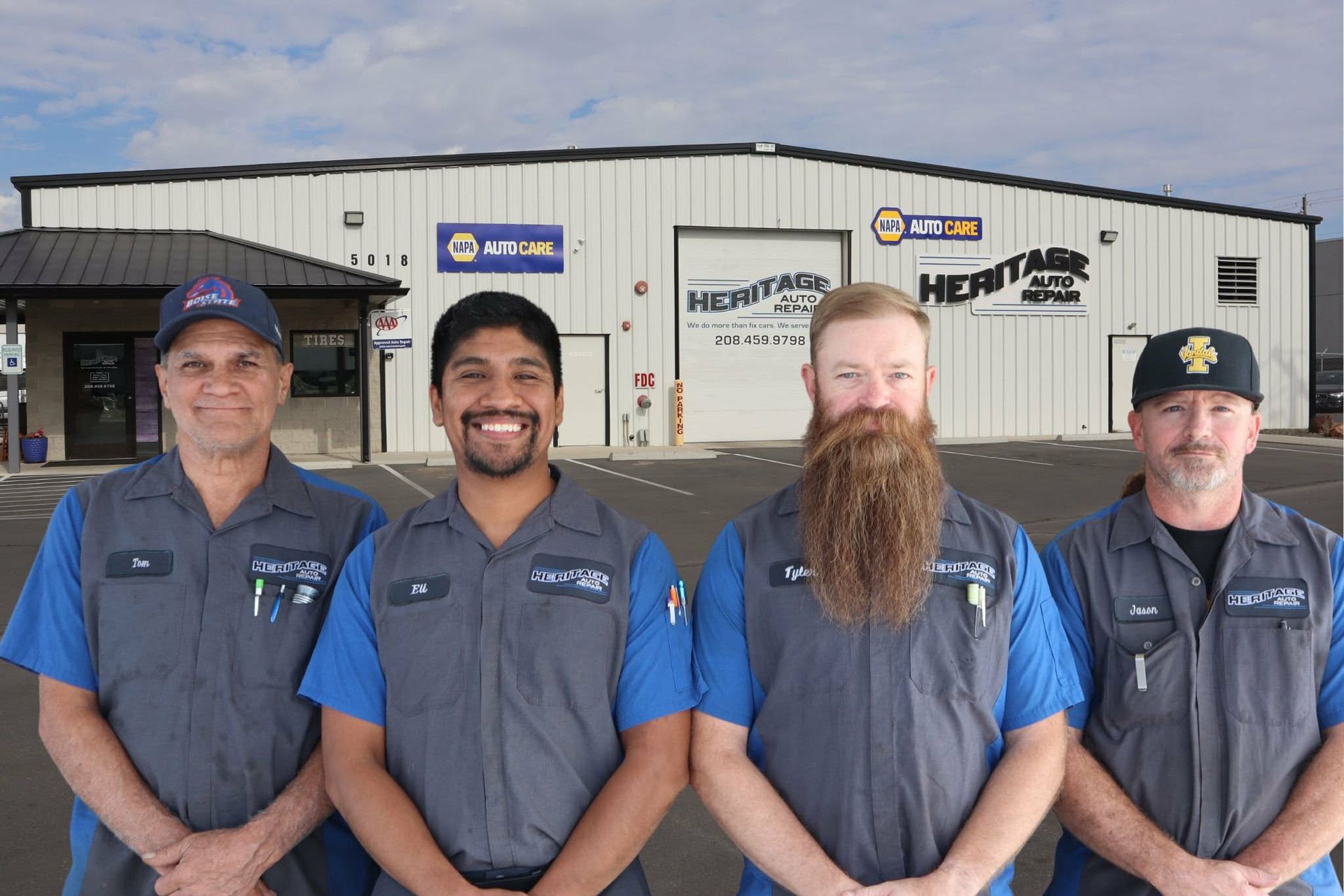 Four mechanics in blue and gray uniforms standing in front of an auto repair shop.