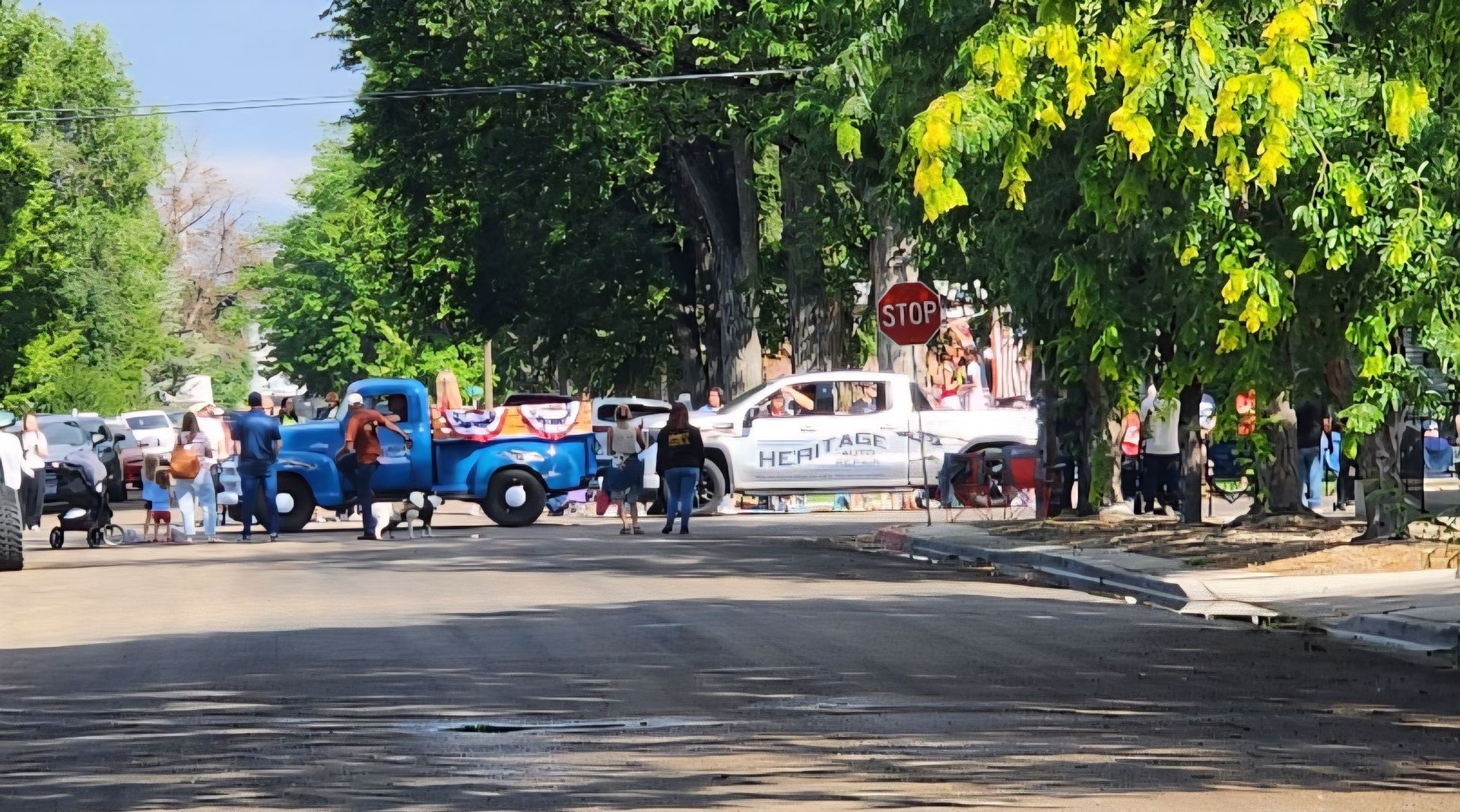 Blue and white utility trucks blocking a tree-lined street, with people standing nearby.