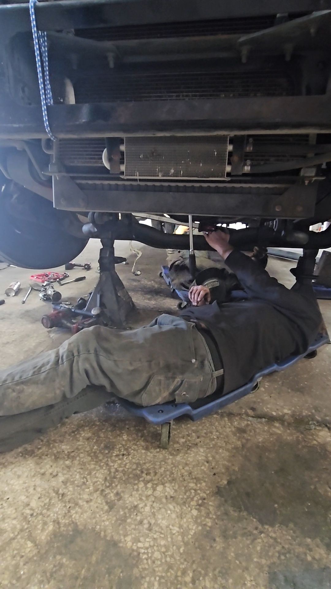 Man working under a vehicle supported by jack stands in a garage.