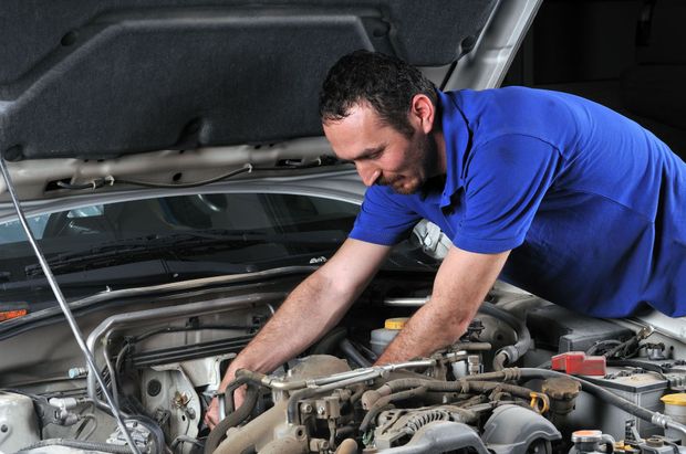 Mechanic in blue shirt working under a car’s hood in a garage