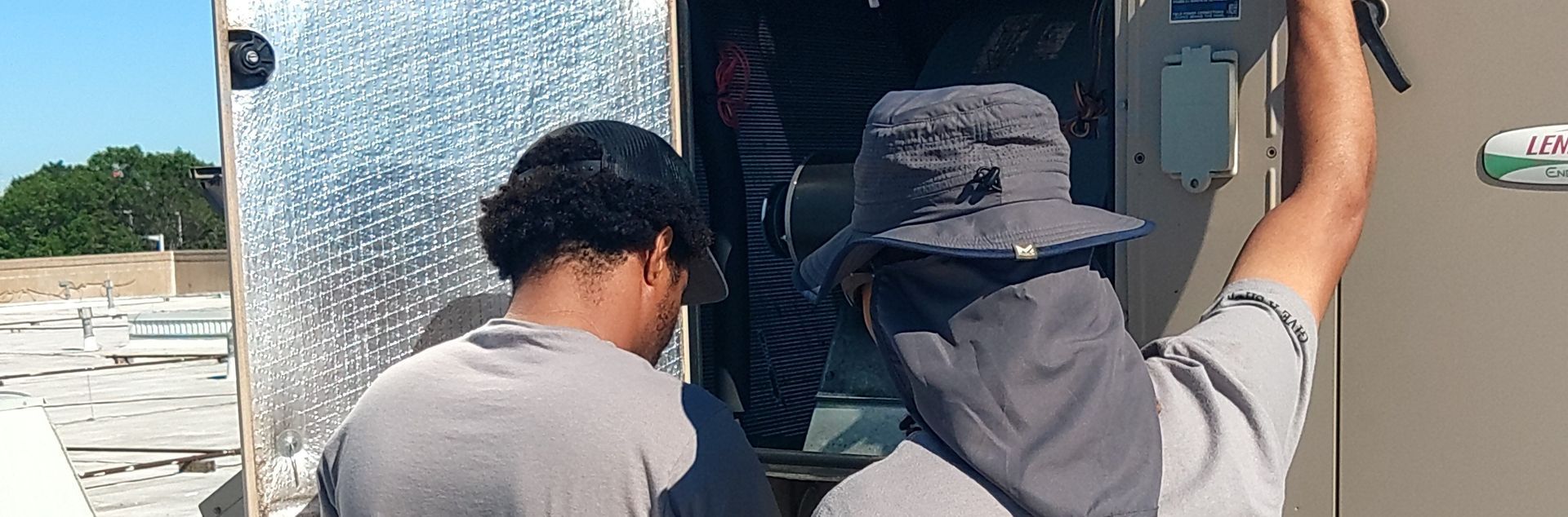 Two people in hats checking the HVAC equipment