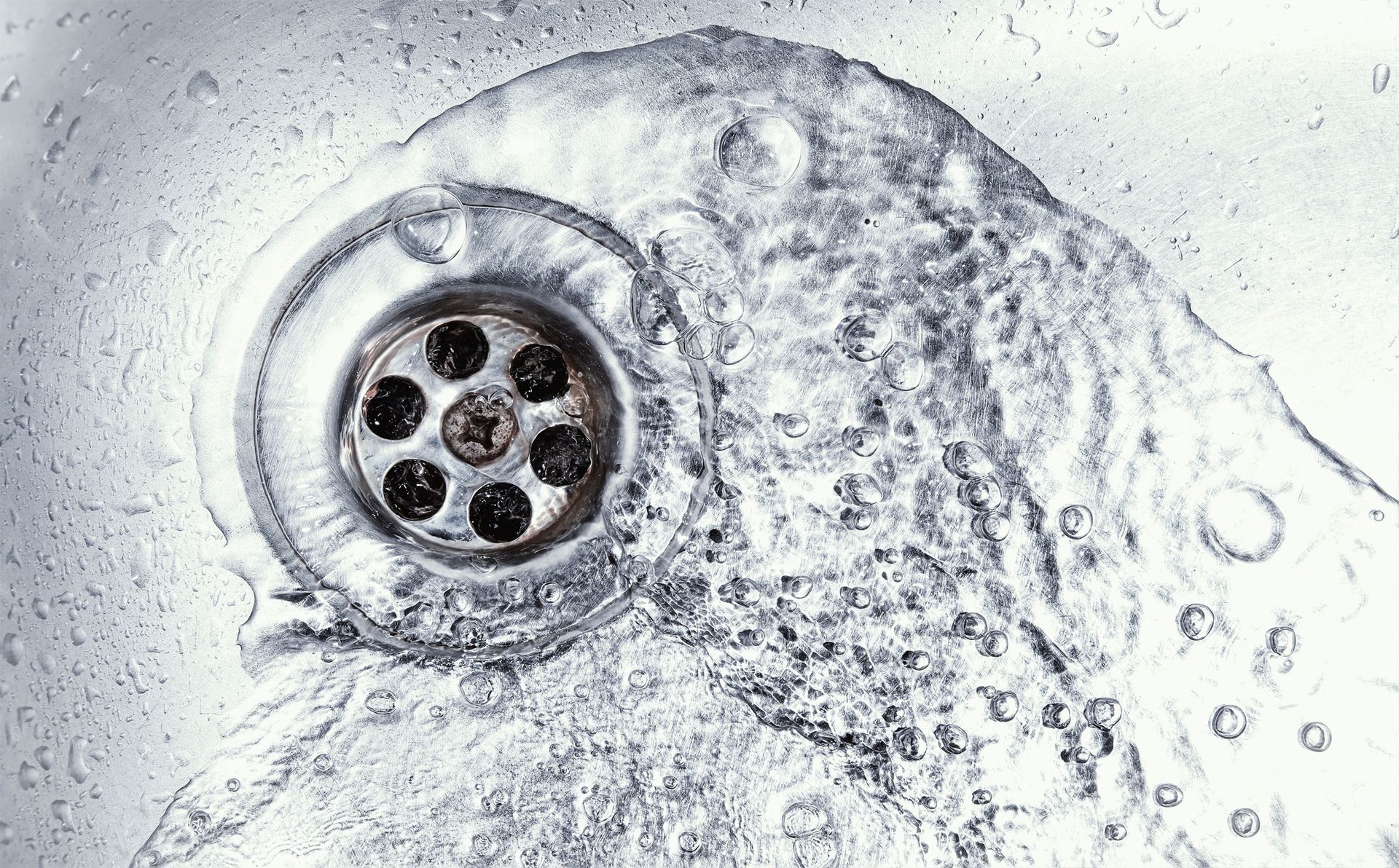 Water flowing down a sink drain; silver sink, swirling water.