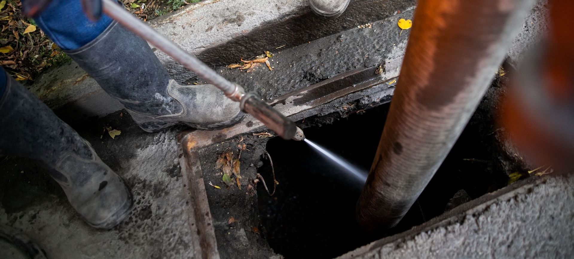 Person in work boots working on a sewer line, using a tool.