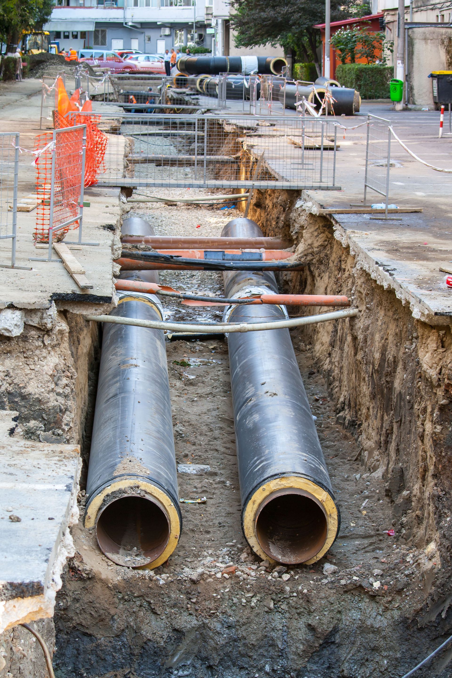 Construction site with large pipes in a trench, orange safety fencing, road work in progress.