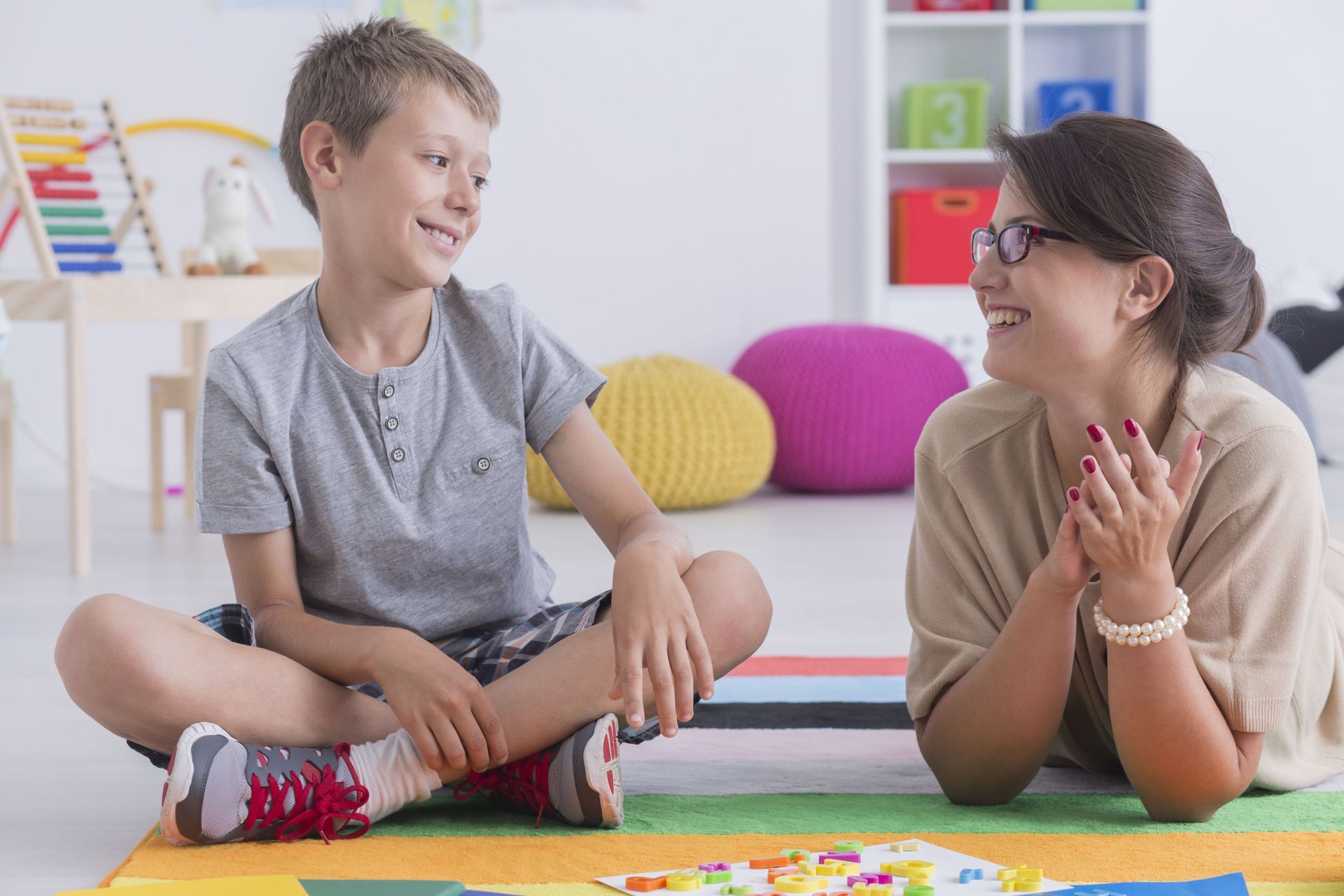 Child and adult lying on floor, smiling and clapping during a playful activity in a bright room
