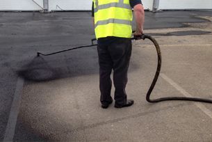 A man in a yellow vest is spraying asphalt with a hose.