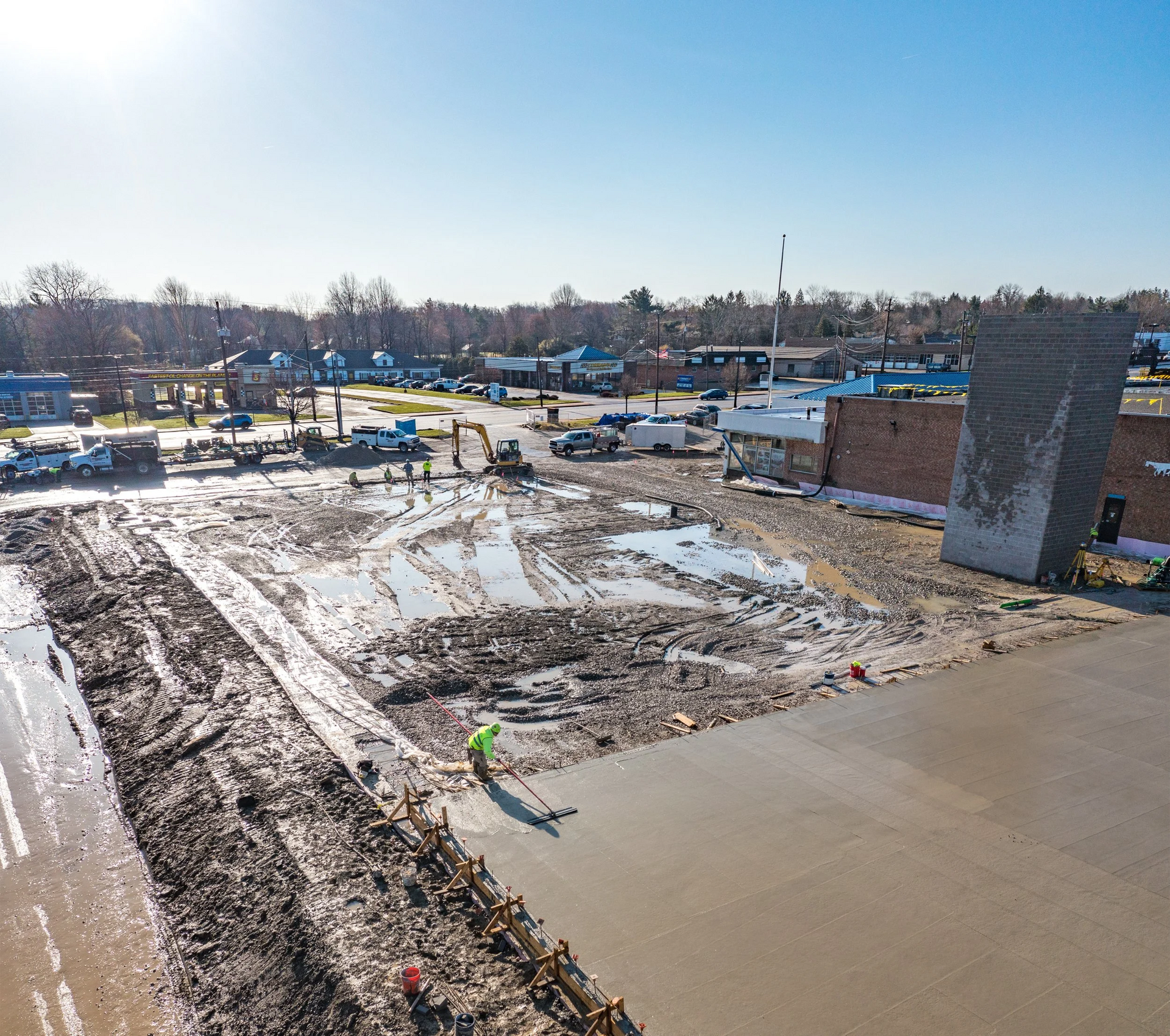 Construction site with concrete foundation, muddy ground, and workers in a snowy suburban area under a clear sky