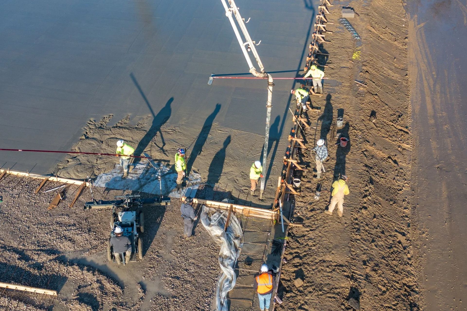 Workers on a muddy riverbank beside a helicopter, securing ropes and equipment near floodwater.