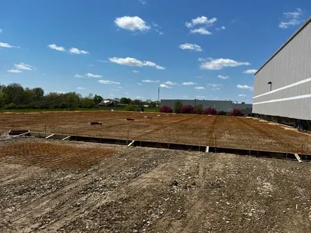 Construction site with graded dirt lot beside a white building under a blue sky
