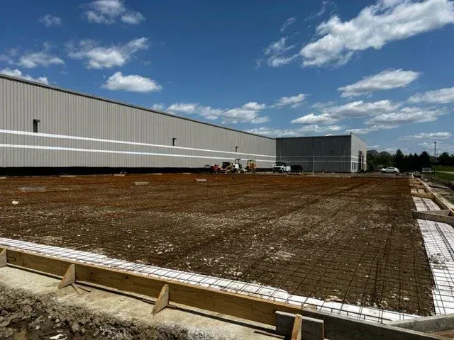 Construction site with rebar foundation and large industrial building under a blue sky