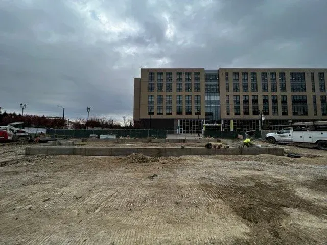 Construction site in front of a large beige office building under a cloudy sky