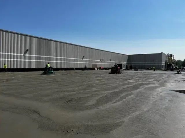 Workers on a flat rooftop near a long gray warehouse under a clear blue sky