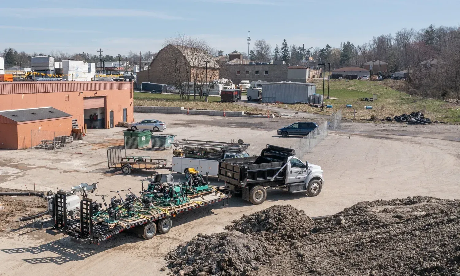 Truck hauling flatbed through an industrial yard with buildings and gravel piles in the background