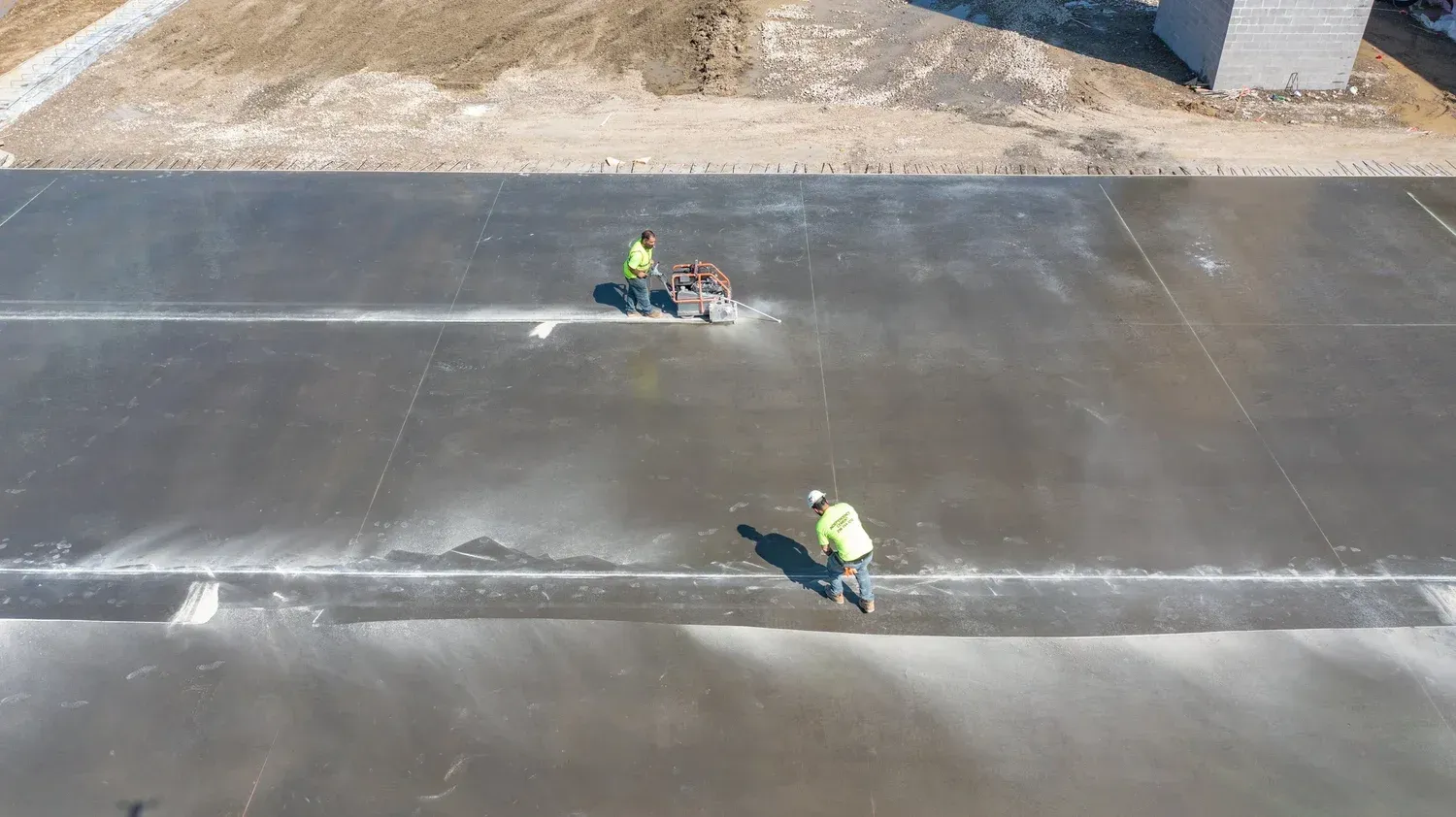 Two workers in neon vests working on a large gray concrete surface outdoors.