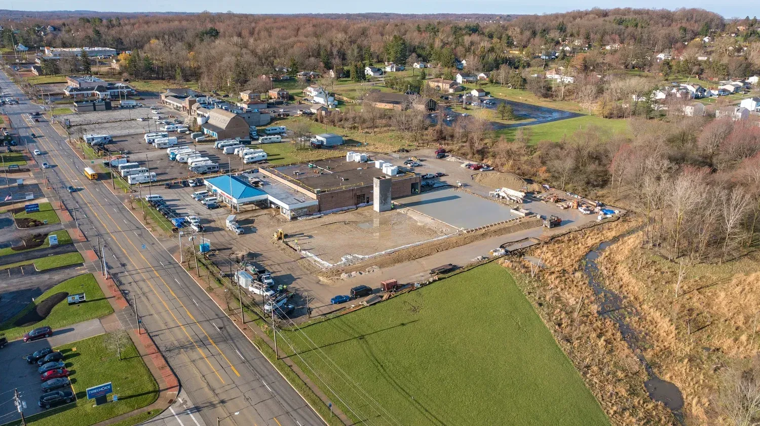Aerial view of a large industrial site with buildings, parking lots, roads, and surrounding trees and fields.