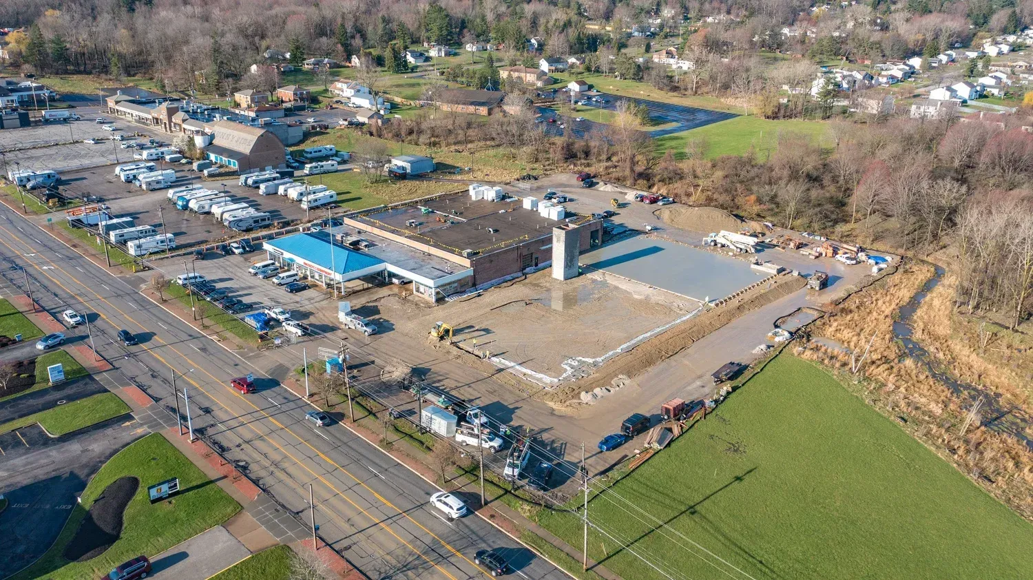 Aerial view of a gas station and parking lot beside a road, with fields and trees nearby.