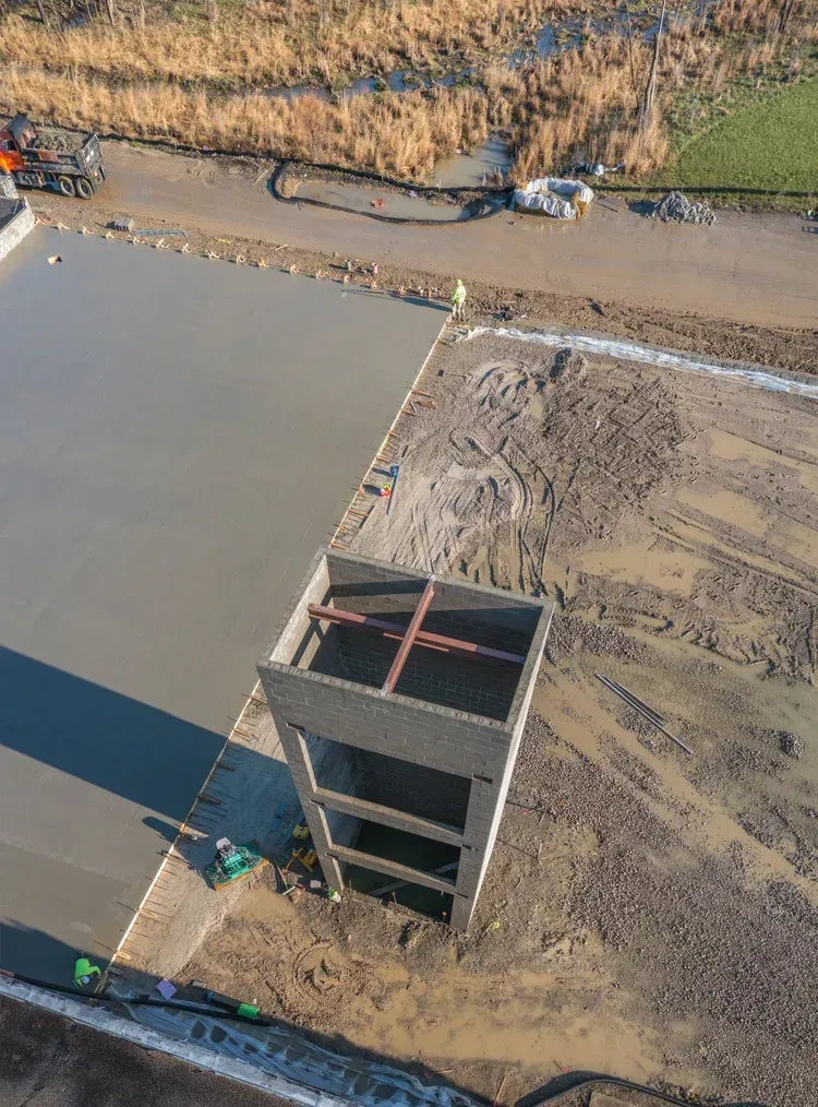 Aerial view of a concrete tower under construction beside a muddy site and roadway.