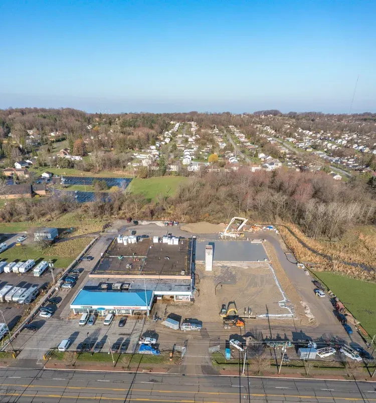 Aerial view of a construction site beside a wooded neighborhood on a clear day