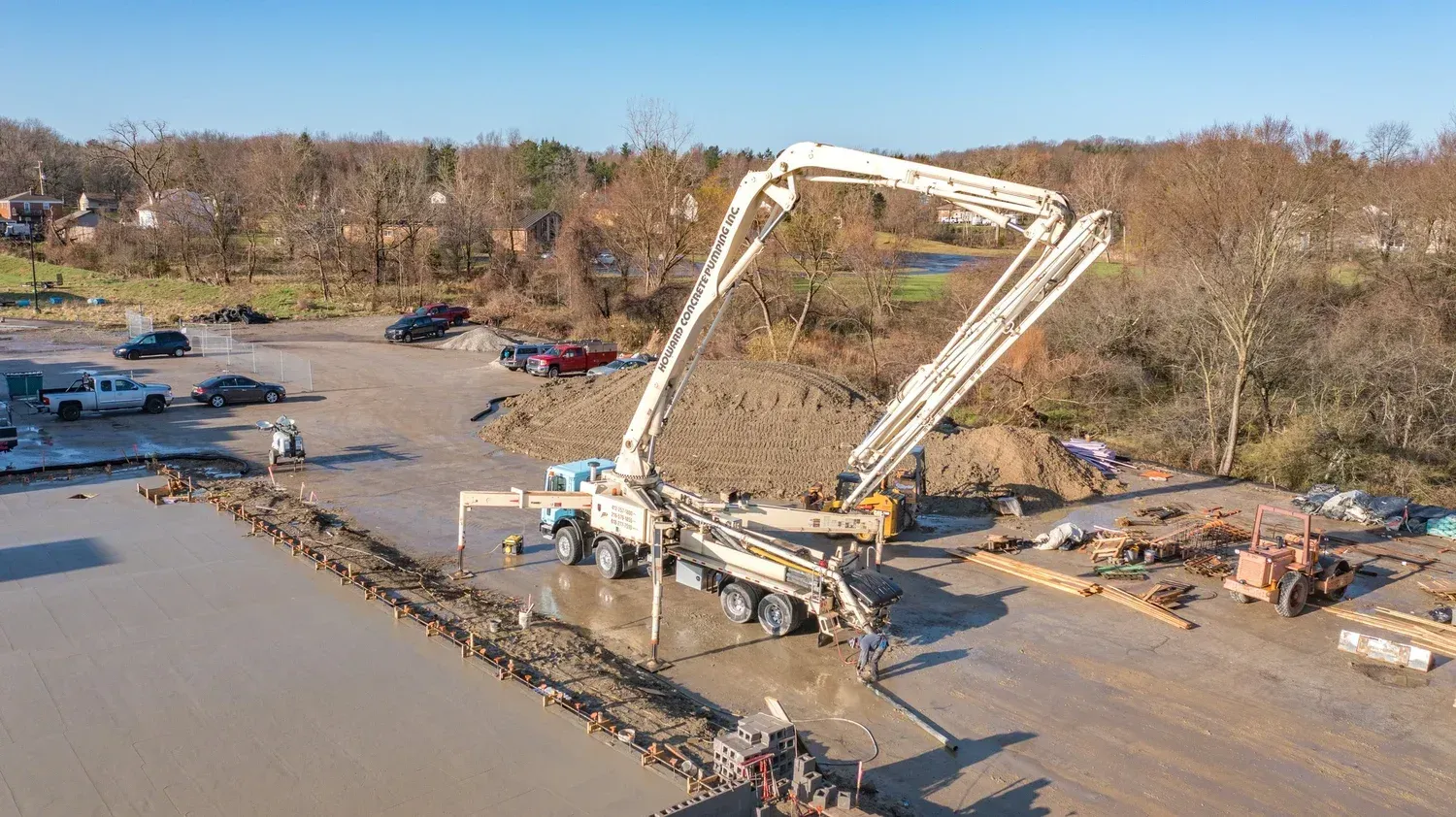 Large concrete pump truck at a muddy construction site with a long white boom extended over the area