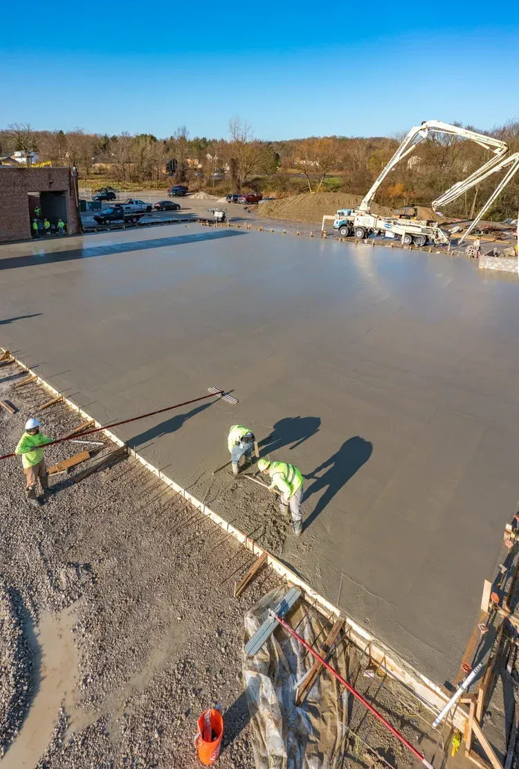 Workers smoothing wet concrete in a large construction site under a blue sky