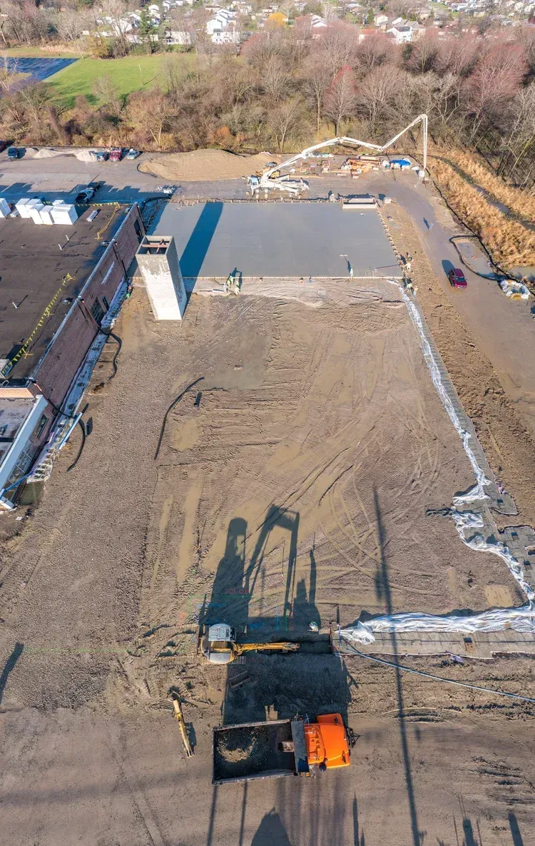 Rooftop construction site with gravel surface, concrete sections, and excavator shadow from above