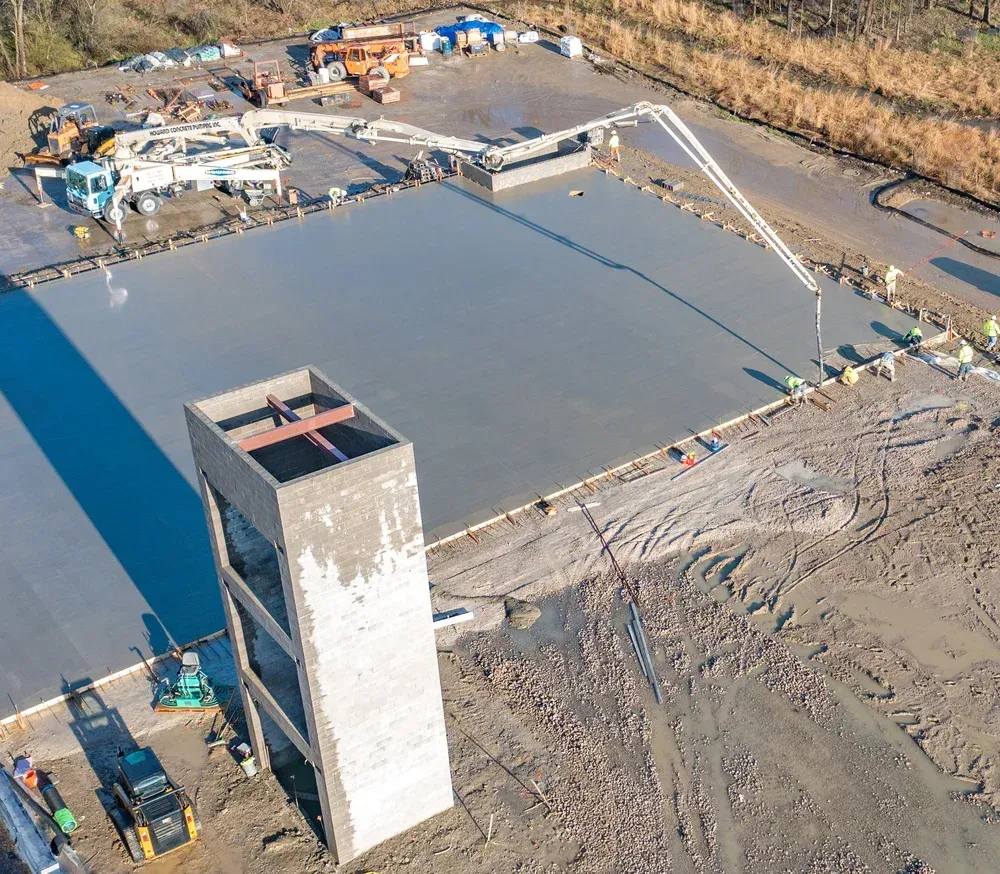 Aerial view of a concrete construction site with a large slab, tower structure, and equipment on muddy ground.
