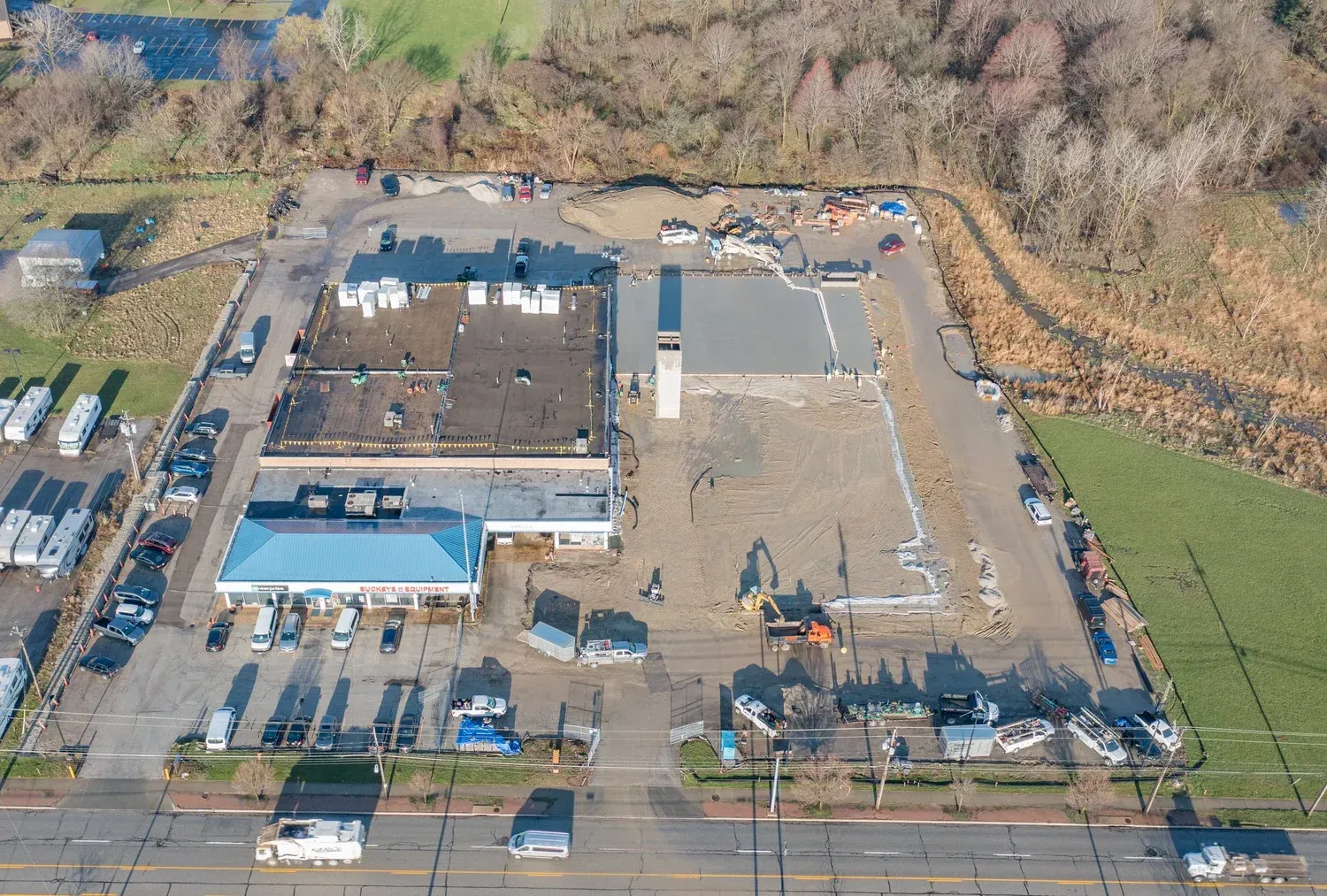 Aerial view of a construction site with large buildings, parked vehicles, and cleared dirt lots near a road.